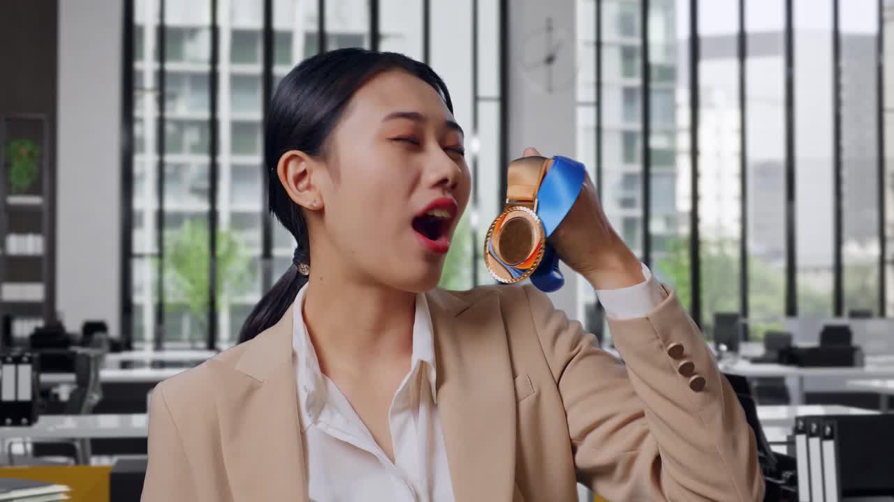 Close Up Of Asian Business Woman In A Suit Kissing A Gold Medal In Her Hand Being Proud Winning As The First Winner In The Office