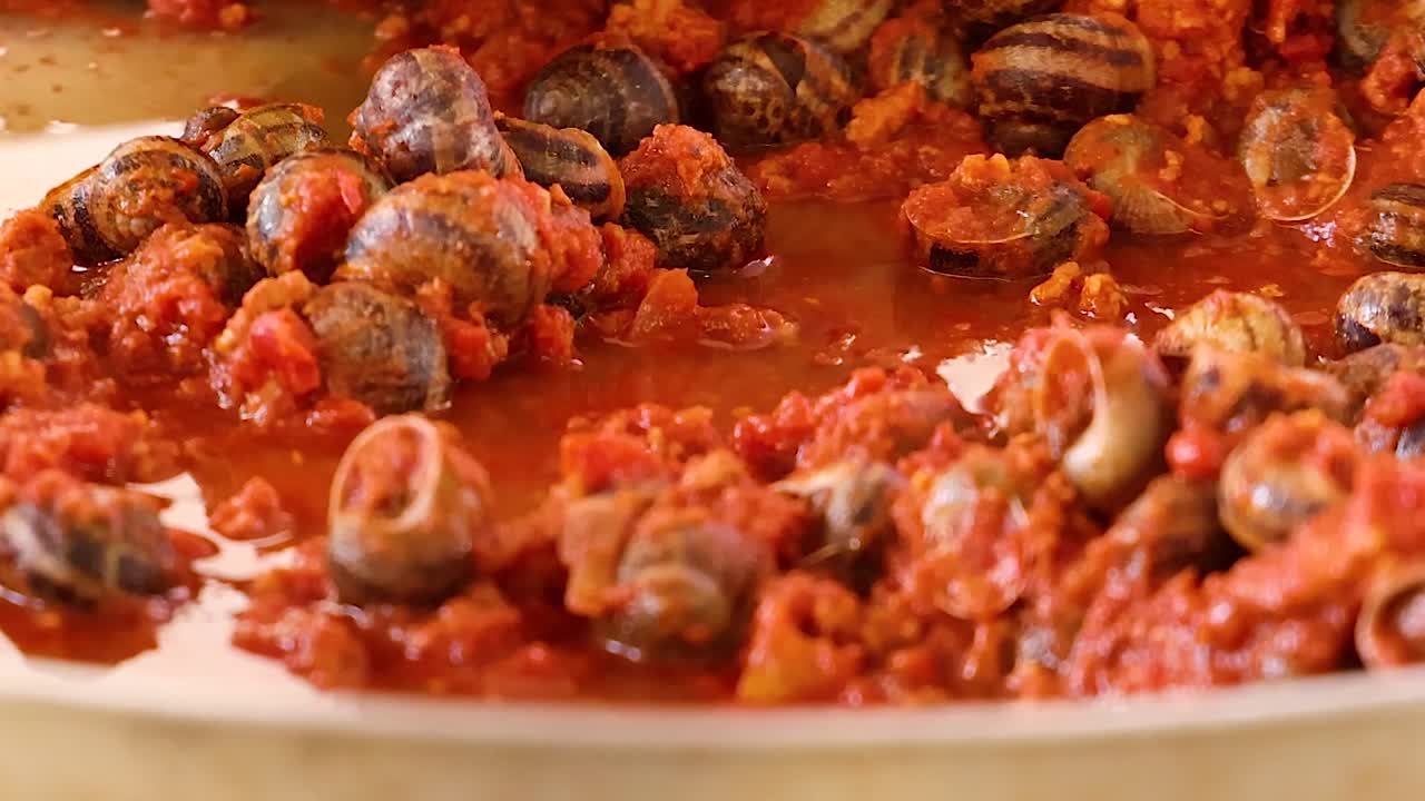 Et detaljeret nærbillede af franske escargot-snegle, der tilberedes i en boblende tomatsauce.