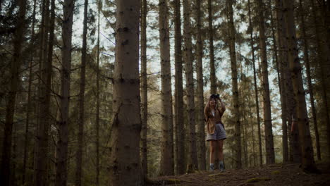 female explorer searching through binoculars amidst trees