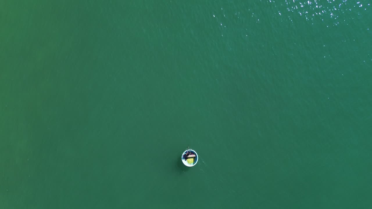 Drone captures turquoise sea from above as a bucket boat with people floats smoothly across the frame, slowly vanishing into the horizon in Mui Ne, Vietnam.