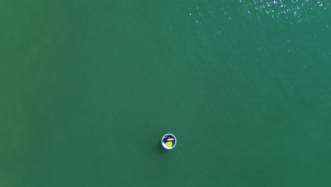 drone captures turquoise sea from above as a bucket boat with people floats smoothly across the frame, slowly vanishing into the horizon in mui ne, vietnam.