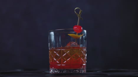 old fashioned cocktail drink chilean version with bourbon whiskey, sugar, ice, bitter dashes, maraschino cherry in dark background and selective focus