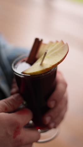 person holding a glass of mulled wine with apple and cinnamon