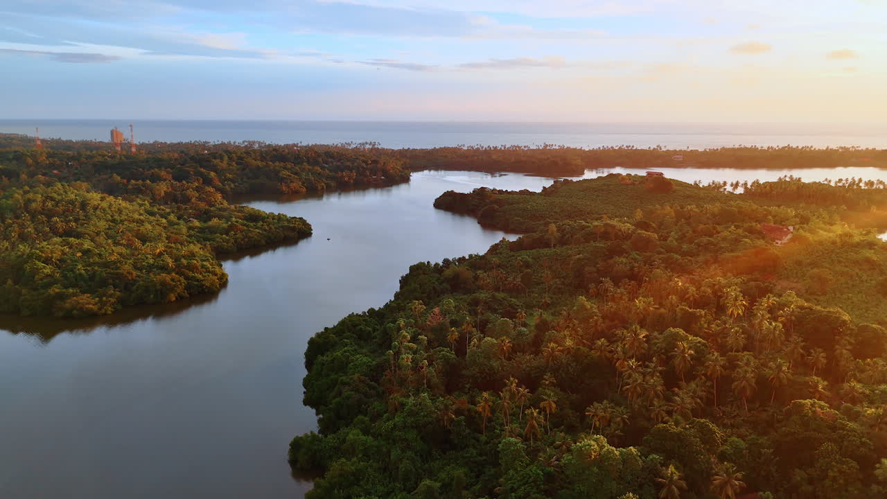 Peaceful river flowing among the tropical forests lit with setting sun rays. Waterscape of the Indian Ocean at backdrop. Aerial perspective.