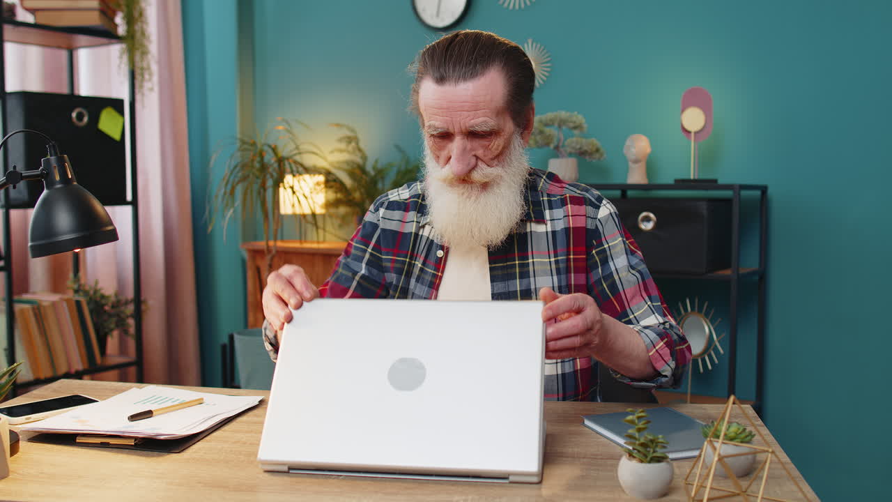 Happy senior man grandfather closing laptop pc computer after finishing work at home office table