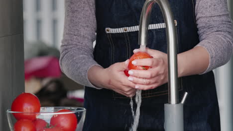 a woman washes ripe tomatoes under a stream of water from a tap