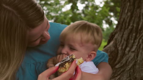 a joyful mother gives her young son a cake to take a bite while embracing him with a smile