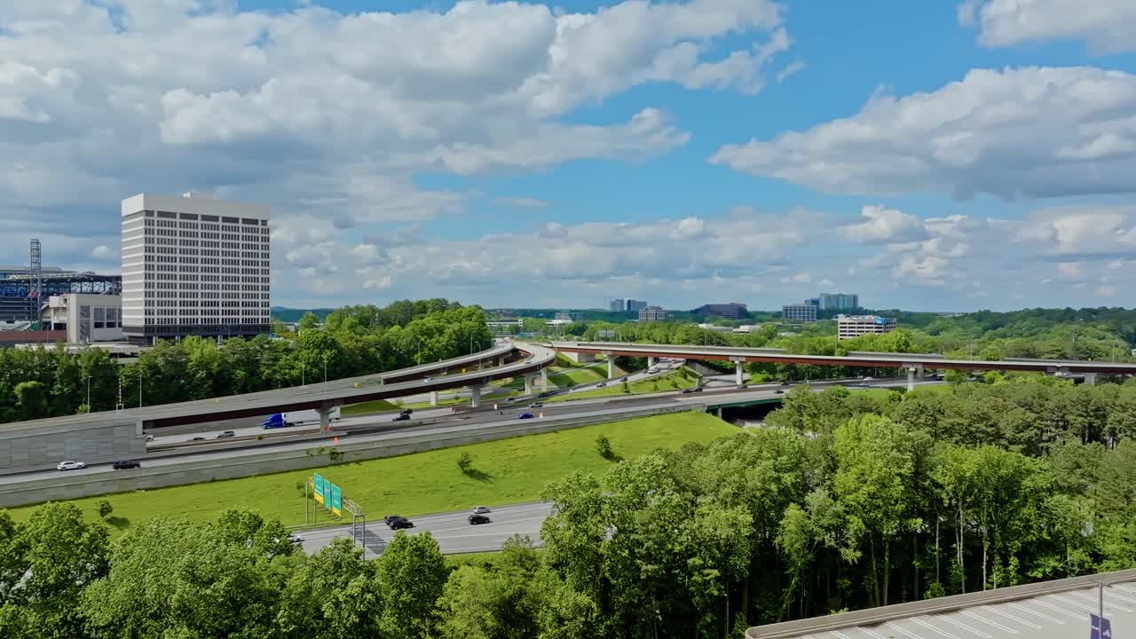 Traffic scene with trucks and cars in american suburb. Overpass highway with green trees and clouds at sky. Aerial wide shot. Office complex block in Atlanta, Georgia.