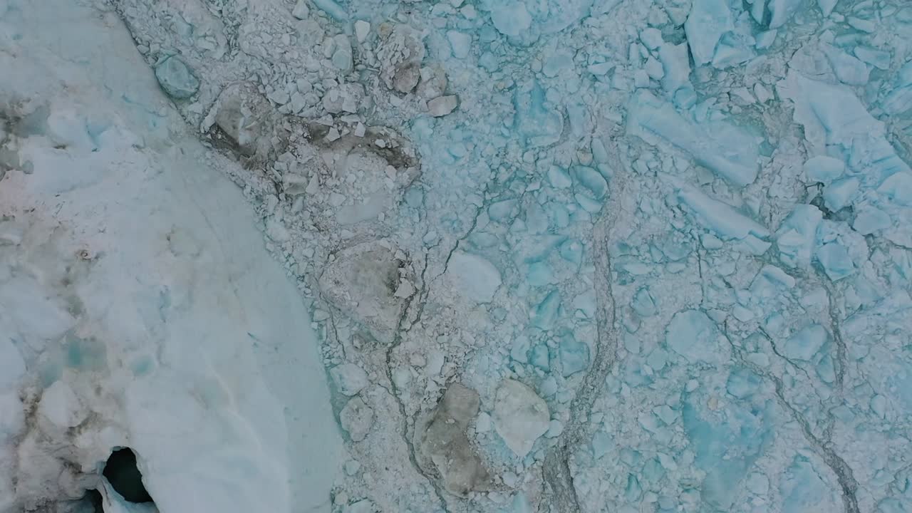 Aerial drone view of fractured blue glacier ice with visible cracks and textures in Greenland, showing natural ice patterns and the frozen beauty of Arctic landscapes