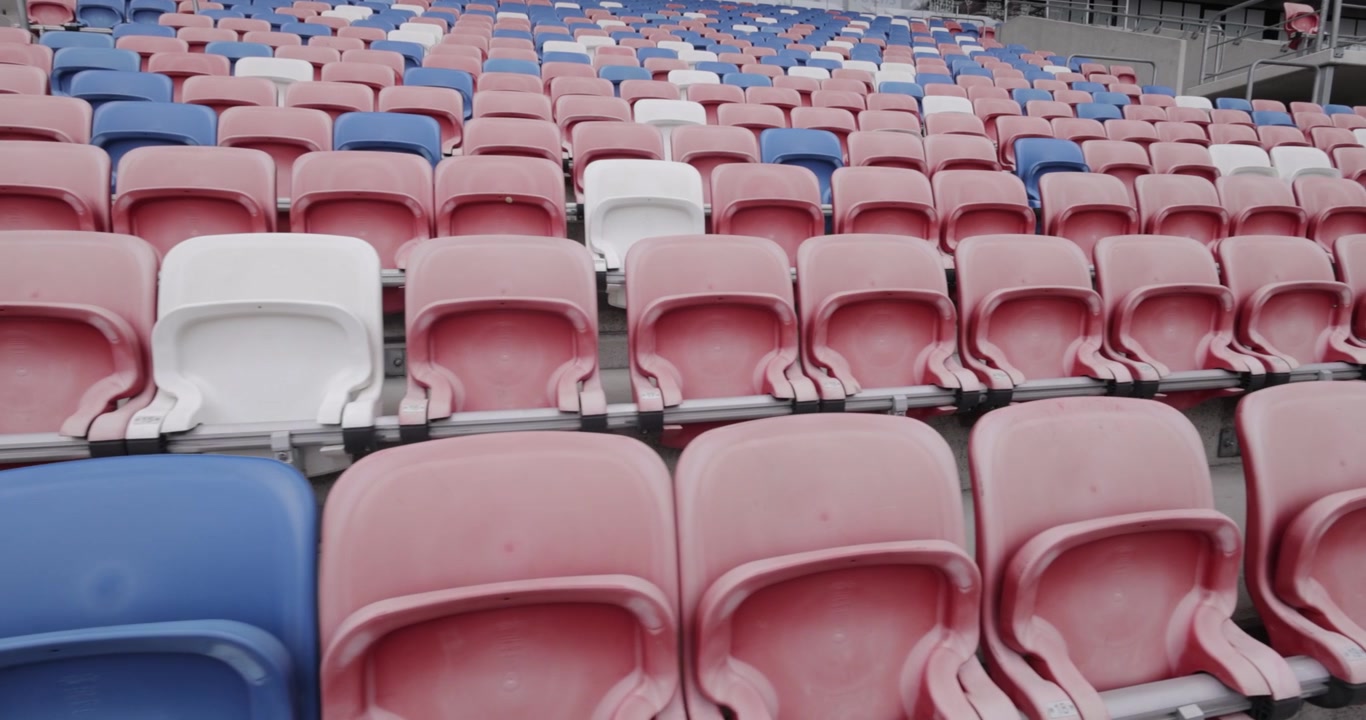 Ripresa dinamica in 4K di lunghe file di sedili vuoti rossi, blu e bianchi in uno stadio di calcio a Zabrze, Slesia, Europa orientale