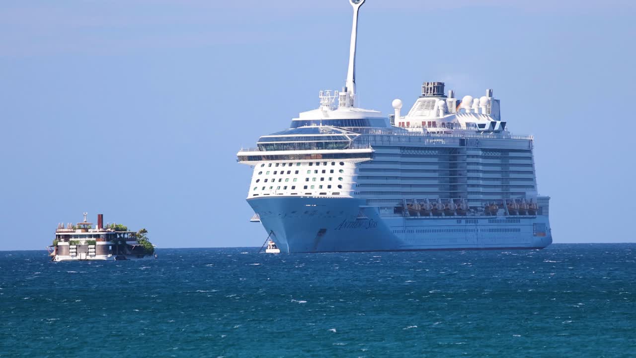 A large cruise ship sails towards Phuket, Thailand, under clear skies, with a smaller boat nearby. Calm ocean setting