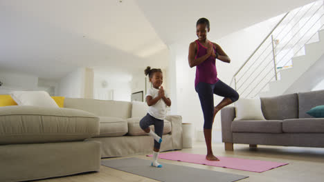 Happy-african-american-mother-and-daughter-doing-yoga-exercise-at-home