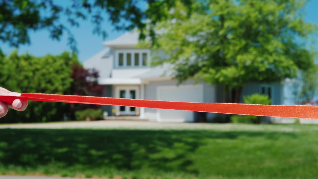 un brazo cortado con tijera corta una cinta roja y una típica casa americana es visible en el fondo housew
