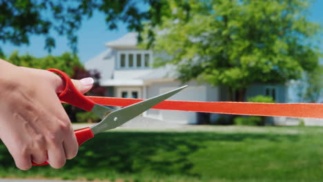 A-Scissor-Cut-Arm-Cuts-A-Red-Ribbon-And-A-Typical-American-House-Is-Visible-In-The-Background-Housew