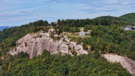 drone approaches chapel and large american flag on the top of the glassy cliffs in landrum, sc.