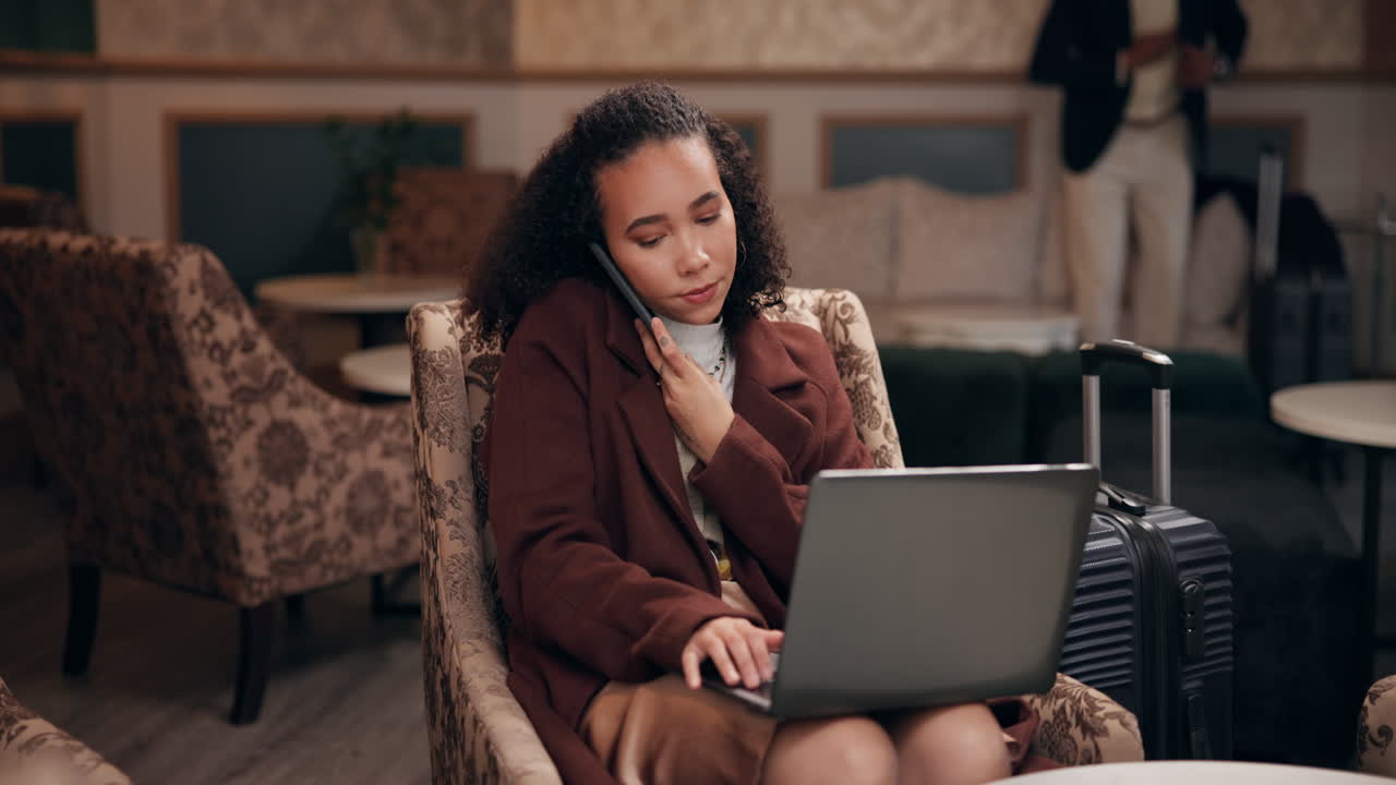 Woman working on laptop and talking on cell phone in hotel lobby