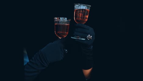 wine in glass in hands on black background. charming female hands in black gloves holding two glasses with red drink. enigmatic atmosphere.