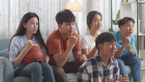 아시아 십대들이 농구 경기를 tv에서 지켜보고 집에서 승리를 축하하고 있습니다.