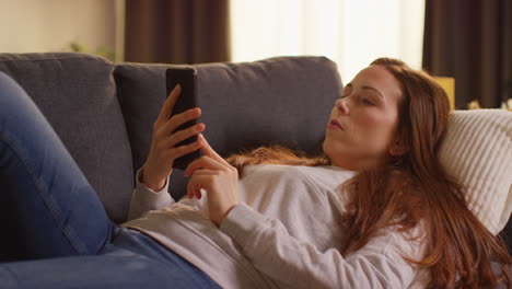 close up de una mujer acostada en el sofá en casa en streaming o viendo una película o un programa o desplazándose por internet en el teléfono móvil 7