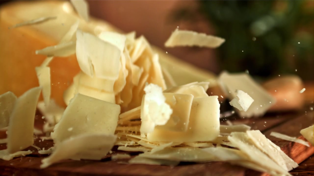 Parmesan Cheese Flakes Falling onto a Wooden Cutting Board in Slow Motion