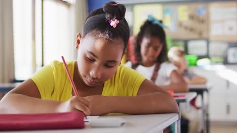 Retrato-De-Una-Colegiala-De-Raza-Mixta-Sentada-En-El-Aula,-Tomando-Notas