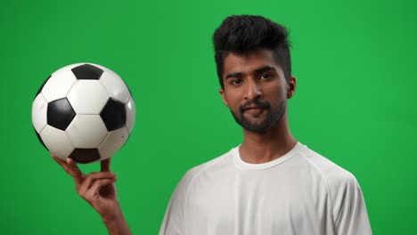 middle eastern footballer looking at ball in hand and looking at camera smiling. portrait of confident handsome bearded sportsman posing at chromakey green screen background.
