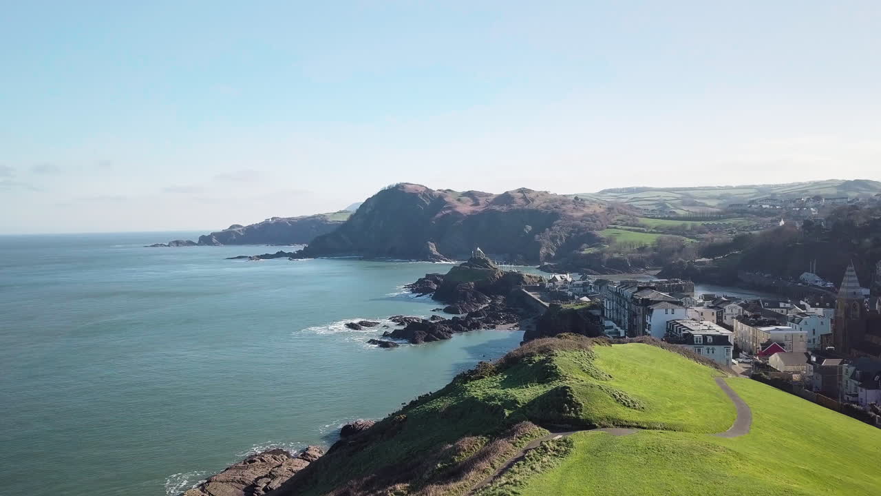 sobrevolando la exuberante colina verde de capstone en un día soleado con vistas al puerto y a la ciudad costera de ilfracombe, costa norte de devon, inglaterra, reino unido