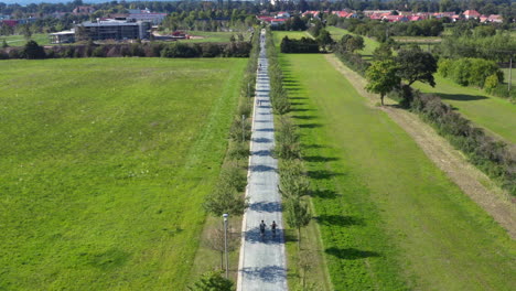 Pareja-En-Bicicleta-Lado-A-Lado-En-La-Carretera-Del-Pueblo-Rural,-Disparo-De-Drones