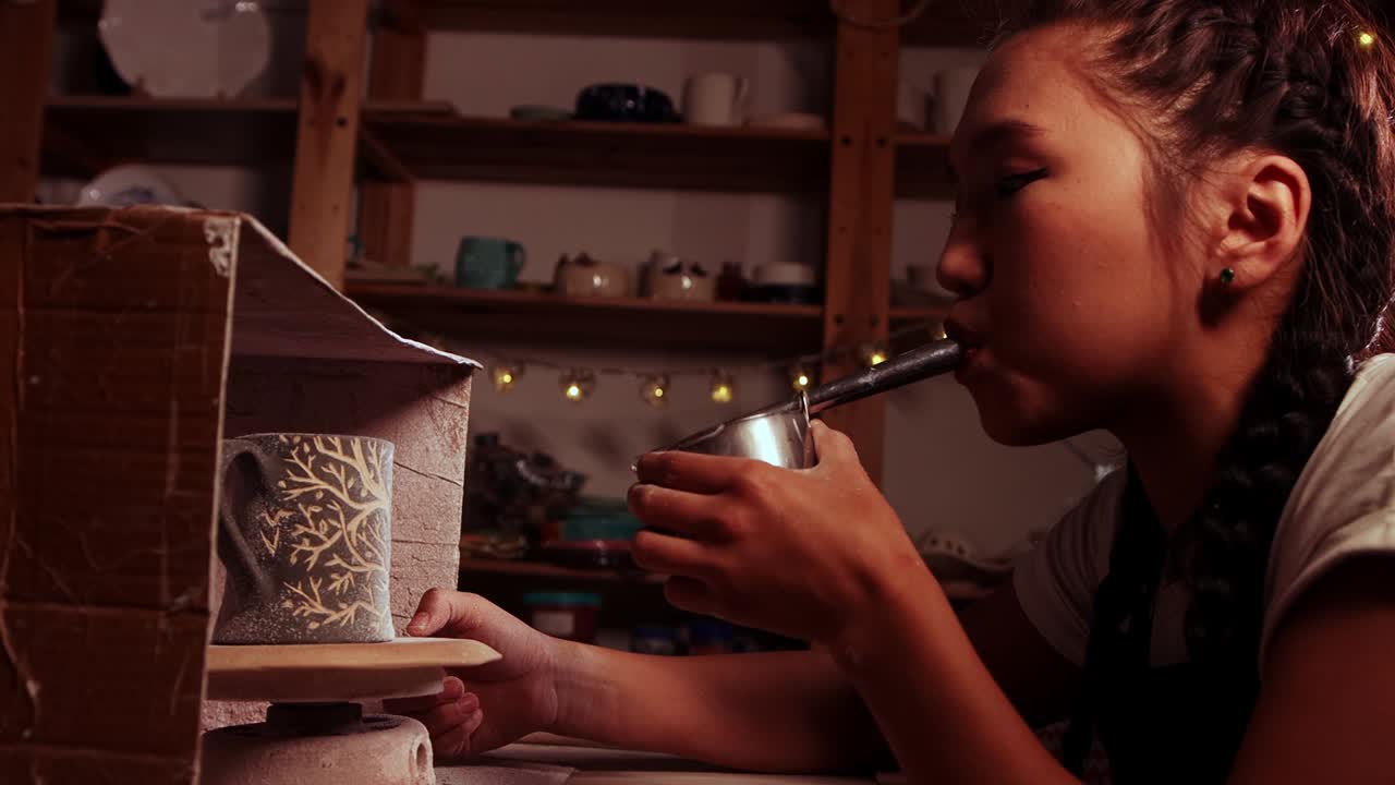 cerámica en el estudio - la mujer alfarera rocia manualmente la pintura soplando en el dispositivo