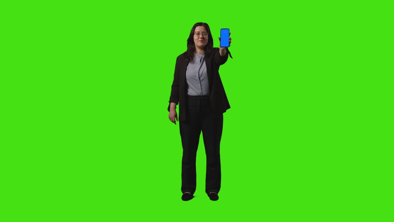 Full Length Shot Of Businesswoman Holding Blue Screen Mobile Phone Towards Camera Standing Against Green Screen