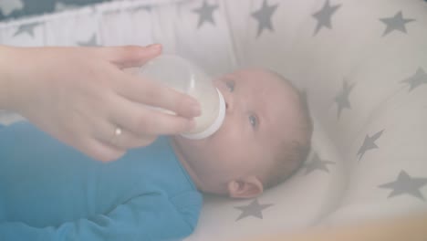 newborn kid eats milk mix from bottle held by mom in cocoon