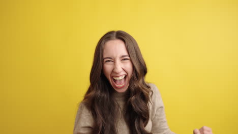 excited young woman celebrating with enthusiasm on yellow background