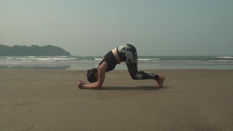 mujer joven en forma practicando una pose de delfín de yoga, ardha pincha mayurasana, en una cálida playa tropical