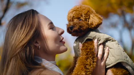 woman holding and smiling at her cute toy poodle puppy in an autumn park