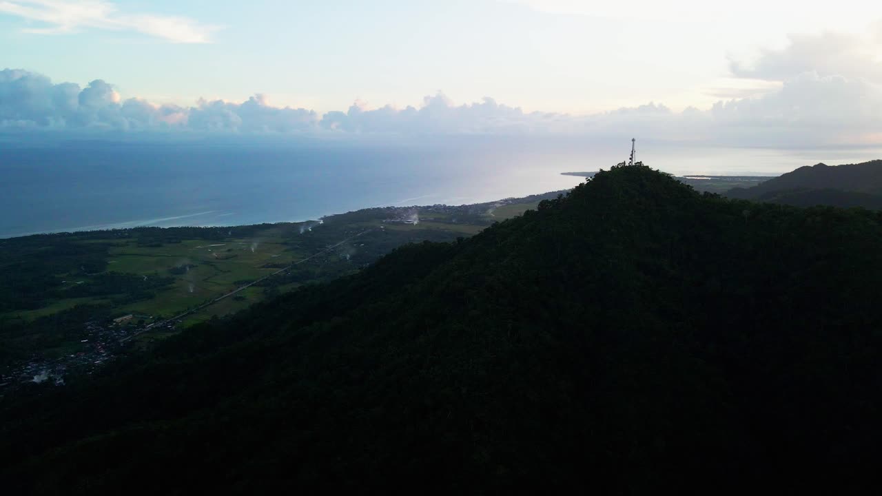 Stunning silhouette of telecommunications tower atop lush Mount Cagmasuso, Catanduanes, overlooking tropical island villages during dusk - aerial view