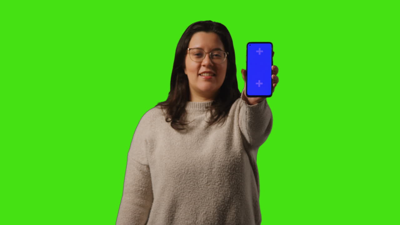 초록색 화면 배경에 서 있는 청색 화면 휴대전화를 들고 있는 젊은 여성의 스튜디오