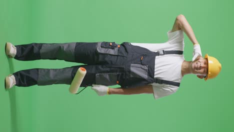 full body of asian man painter wearing safety helmet smiling and making call me gesture to camera while standing in the green screen background studio