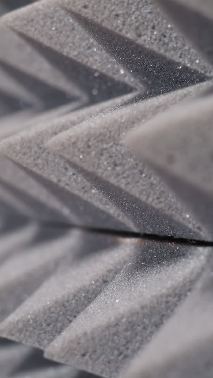 primer plano íntimo de paneles de espuma acústica en forma de pirámide gris, capturando la textura y los reflejos de luz ideales para configuraciones de audio profesionales