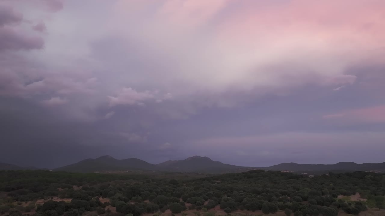 Drone flight turning left over the head of the Tiétar Valley,revealing forested landscapes and mountains of the Central System. A dramatic sky with storm clouds shows violet,pink, gray and white tones