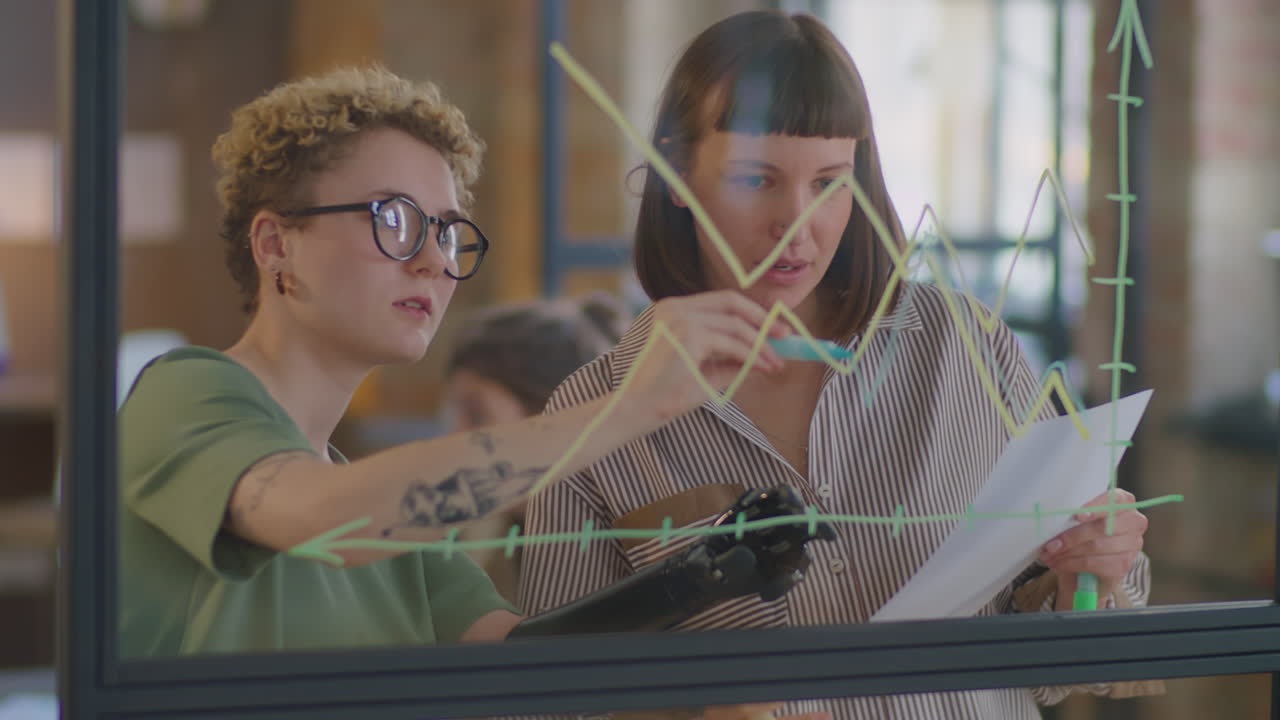 Woman with Prosthetic Arm Drawing Graph on Glass Wall with Colleague