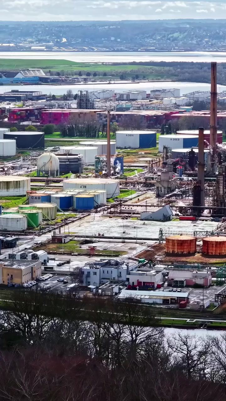 Wide aerial view revealing large industrial refinery with storage tanks and chimneys