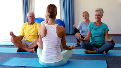 Trainer-assisting-senior-citizens-in-practicing-yoga