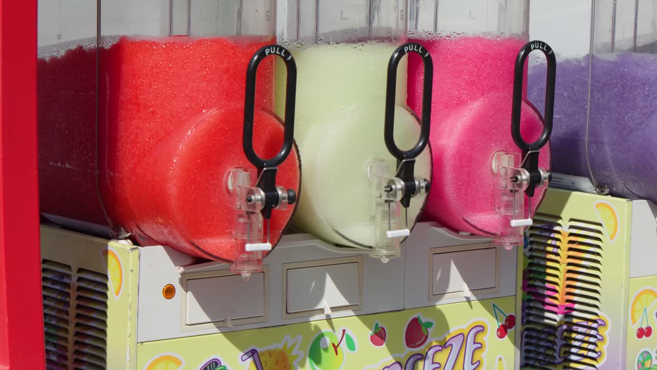 Four vibrant slush dispensers mix fruit flavors in bright daylight at a French outdoor setting