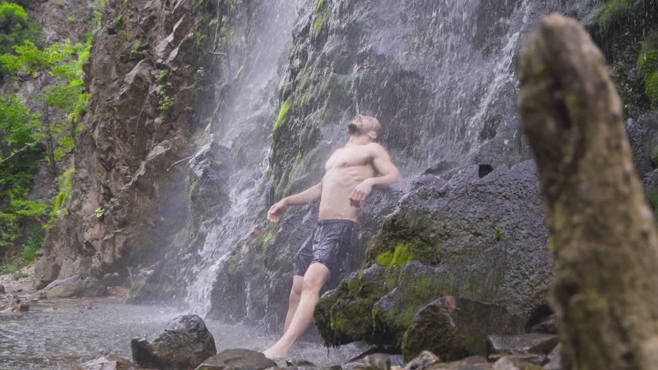 сильный человек опирается на скалы под водопадом.