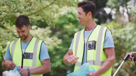 diverse group of male and female friends with blue refuse sacks in forest and high fiving