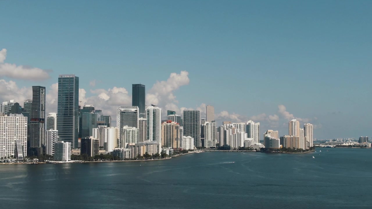 Amplia vista aérea del horizonte del centro de Miami volando sobre el agua y un puente en 4K.
