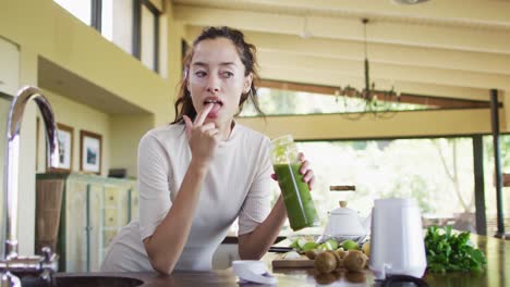 Glückliche-Biracial-Frau-Mit-Vitiligo,-Die-Smoothie-Aus-Den-Fingern-In-Der-Küche-Schmeckt