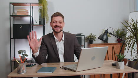 Businessman-working-on-laptop-smiling-friendly-at-camera-and-waving-hands-gesturing-hello-at-office