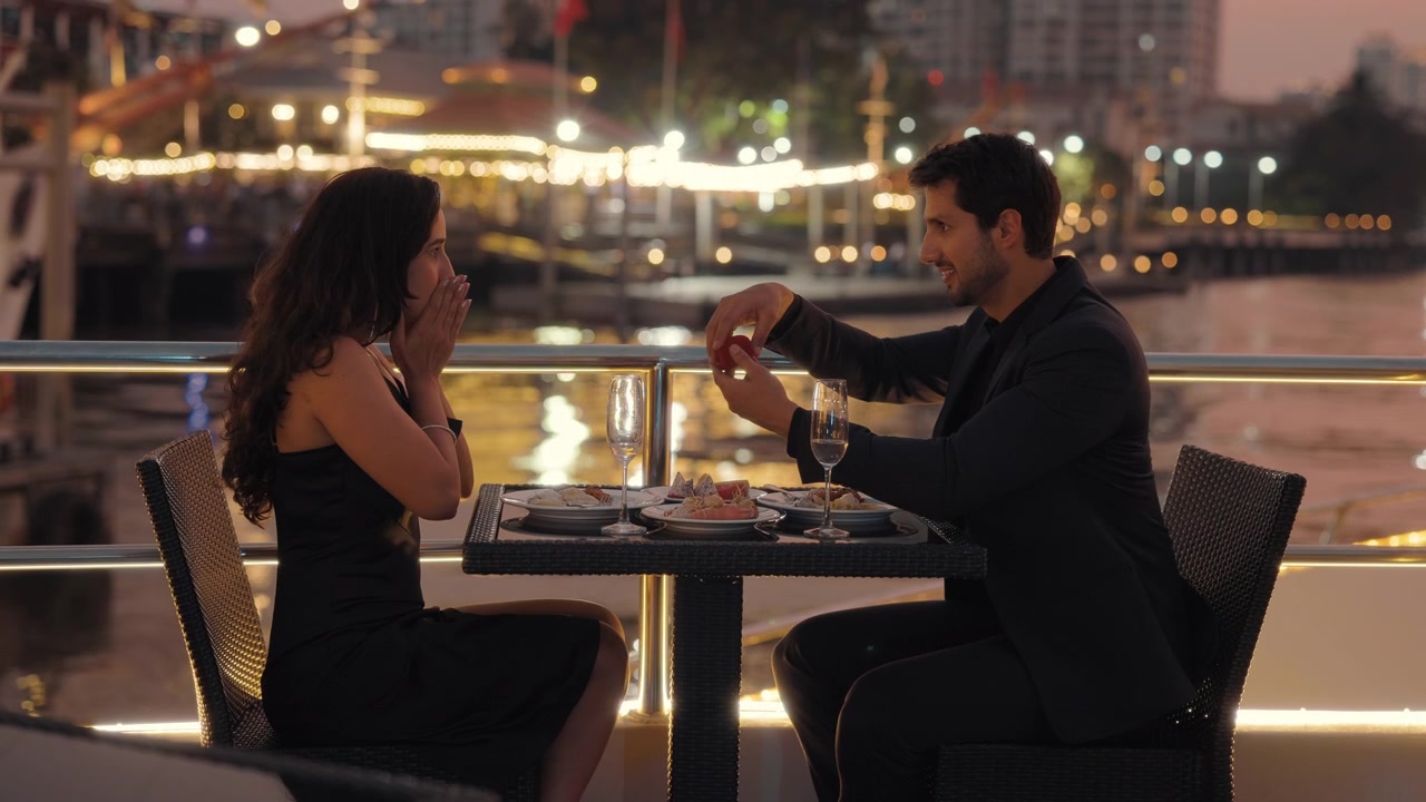 Uomo che fa la proposta di matrimonio a una donna con un anello di fidanzamento durante una cena romantica su uno yacht.