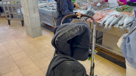 a person with a baby stroller is browsing the fish market, surrounded by fresh seafood. the scene captures the everyday activity of shopping for fresh ingredients in a bustling local market.